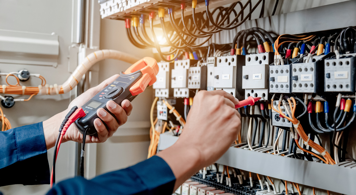 Electrician verifying system performance and troubleshooting wiring issues in a commercial electrical cabinet